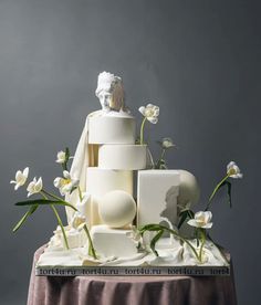 a cake with white flowers on it and a statue in the middle surrounded by other cakes