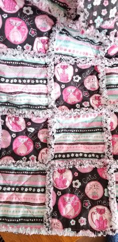 a pink and black patchwork quilt with hearts on it's edges, sitting on a wooden table