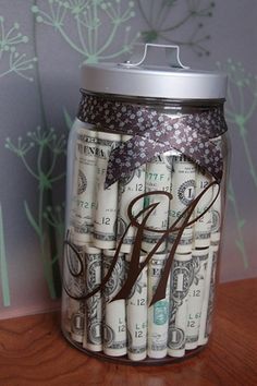 a glass jar filled with money sitting on top of a wooden table next to a wall