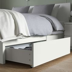 a bed with two drawers underneath it on the floor next to a night stand and lamp