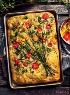 a square casserole with tomatoes and herbs on top, next to a glass of wine