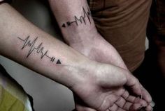 two people holding hands with heartbeat tattoos on them