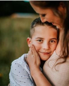 a young boy is hugging his mother's shoulder while she smiles at the camera