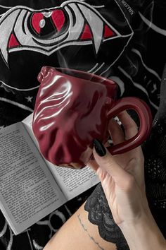 a woman is holding a red coffee mug in her left hand and reading a book