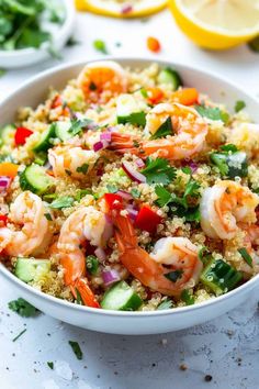 a bowl filled with shrimp and couscous next to lemon wedges on the side