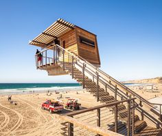 a lifeguard station on the beach with people and vehicles parked in front of it