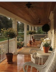 a porch with wicker chairs and potted plants on the front porch, along with a wooden floor