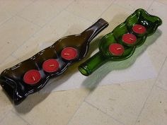 two green bottles sitting on top of a counter next to each other with red candles in them