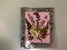 a silver frame with flowers and leaves on a pink wall in a room that has white walls