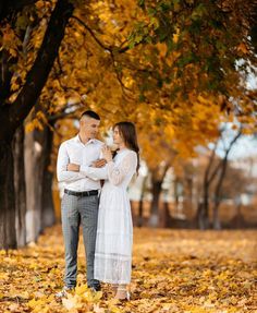 a man and woman are standing in the leaves under a tree with their arms around each other