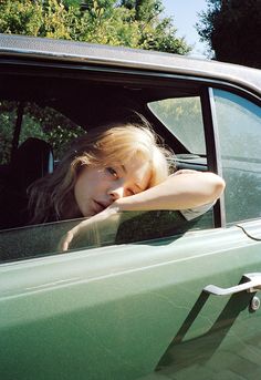 a woman leaning her head out the window of a green truck with trees in the background