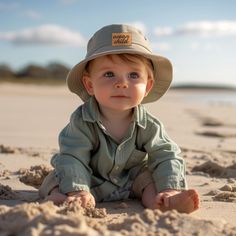 a little boy sitting in the sand wearing a hat and looking up at the camera