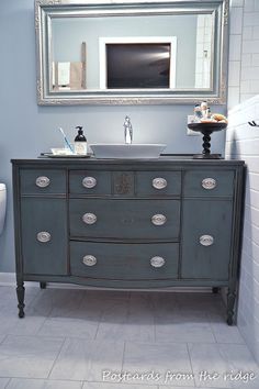 a bathroom with a sink, toilet and blue painted dresser in it's corner