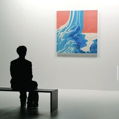 a person sitting on a bench in front of a painting with blue and red waves