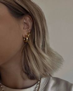 a woman with blonde hair wearing large gold hoop earrings and a white sweater is looking off to the side