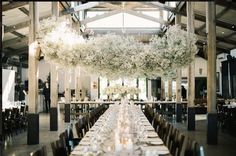 the tables are set for an event with white centerpieces and flowers hanging from the ceiling