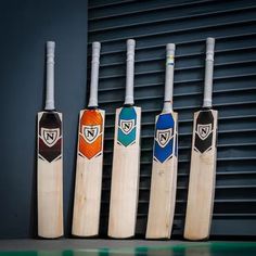 four wooden cricket bats lined up against a wall