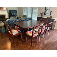 a dining room table with colorful chairs and a blue couch in front of the fireplace