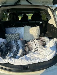 the back end of a white van with pillows and blankets in it's trunk