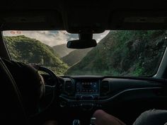 a man driving a car down a road next to a lush green forest covered hillside