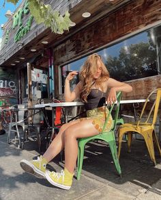 a woman sitting on a green chair in front of a storefront with her legs crossed