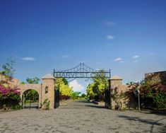 a stone driveway with an iron gate and flowers on the sides, surrounded by brick walls