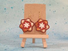 a pair of red and white crocheted flower earrings sitting on top of a wooden stand