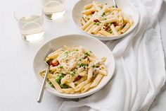 two white bowls filled with pasta and peas on top of a table next to glasses