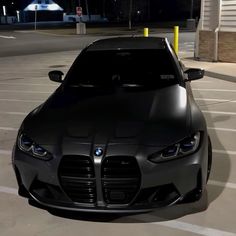 the front end of a black car parked in a parking lot at night with its lights on