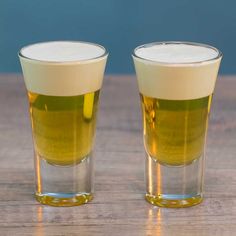 two shot glasses filled with liquid sitting on top of a wooden table