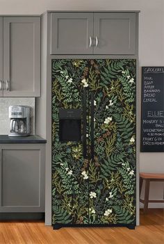 a kitchen with grey cabinets and a black floral wallpaper on the side of the refrigerator