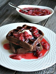 chocolate waffles with strawberries and syrup on a white plate next to a bowl of ice cream