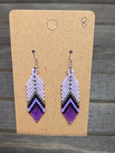 a pair of purple and black beaded earrings sitting on top of a wooden table