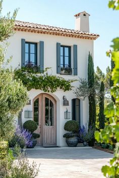 a white house with blue shutters and potted plants on the front door is surrounded by greenery