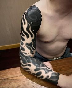 a man with a black and white tattoo on his arm sitting at a wooden table