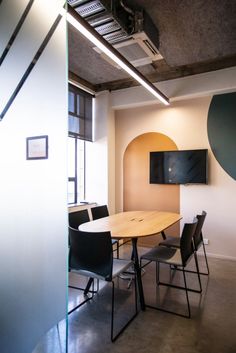 an empty conference room with a round table and black chairs in front of a flat screen tv mounted on the wall