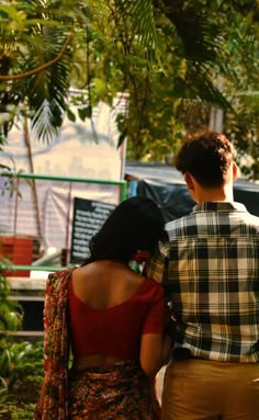 a man and woman standing next to each other in front of some trees looking at something