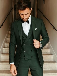 a man wearing a green suit and bow tie standing in front of stairs with his hand on his hip