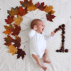 a baby laying on top of a bed next to autumn leaves and bead necklaces