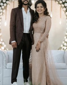 a man and woman standing next to each other in front of a white couch with flowers