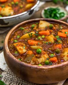 a bowl filled with stew and vegetables on top of a wooden table next to other dishes