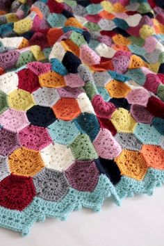 a crocheted blanket is laying on top of a white tablecloth with multicolored squares