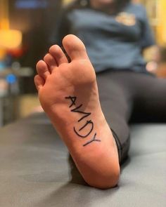 a person with a tattoo on their foot that says sandy in black ink, sitting on a table