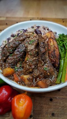 a white bowl filled with meat and vegetables on top of a wooden table next to peppers