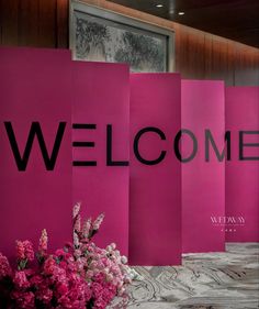 pink paper with the word welcome written on it and flowers in vases next to it