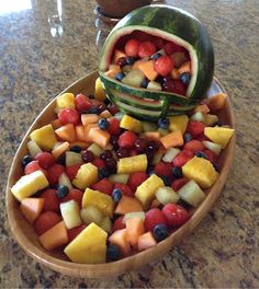 a wooden bowl filled with fruit sitting on top of a counter next to a watermelon