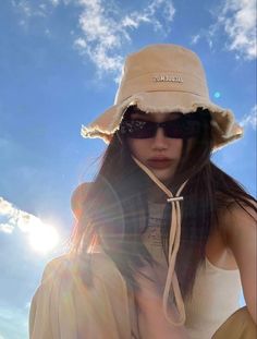 a woman wearing a hat and sunglasses sitting in the sun with her hands on her hips