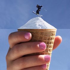 a person holding an ice cream cone with pink nail polish and a skier on top