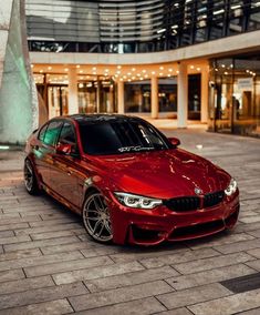 a red bmw car parked in front of a building with lights on it's windows