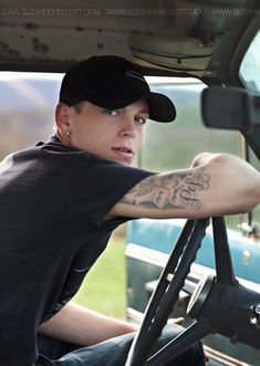 a man sitting in the driver's seat of a truck with tattoos on his arm